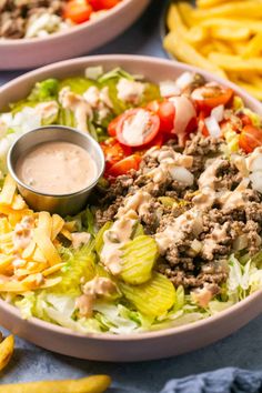 two bowls filled with salad and fries on top of a blue table cloth next to each other