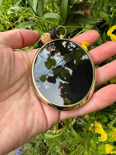 a hand holding a small round mirror in front of some flowers