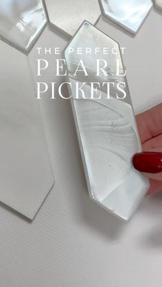 a woman's hand with red nail polish holding a piece of white marble in front of some hexagonal tiles