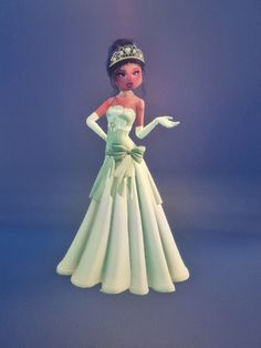 a doll wearing a green dress with a tiara on it's head and hands in her other hand