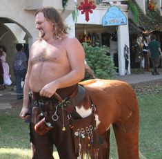 a man with no shirt standing next to a brown and white horse in the grass