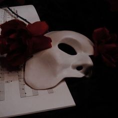 a white mask sitting on top of sheet music with red flowers in it's mouth