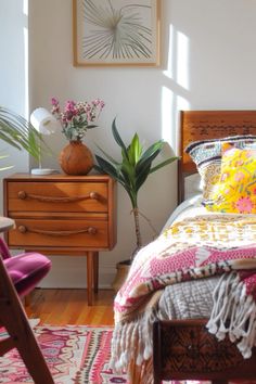 a bed room with a neatly made bed next to a wooden dresser and two planters