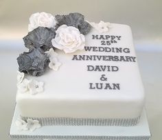 a white and gray wedding cake with flowers on the top is decorated with words that read happy 25th wedding anniversary david & luan