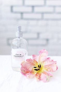 a pink flower sitting next to a bottle of water on top of a white table