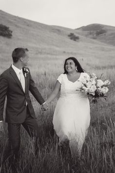 a bride and groom holding hands walking through tall grass