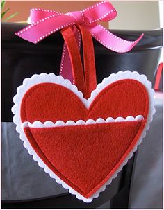 a red felt heart hanging from a chair with a pink ribbon on it's edge