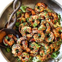 a pan filled with cooked shrimp and broccoli next to a wooden spatula