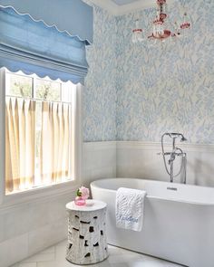 a white bathtub sitting next to a window in a bathroom under a chandelier