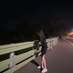 a woman leaning against a rail on the side of a road at night with her hair blowing in the wind