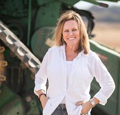 a woman is standing in front of a green tractor with her hands on her hips