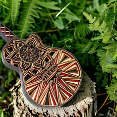 a wooden guitar sitting on top of a tree stump next to green plants and leaves