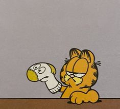 garfield the cat is holding an object in his hand while sitting at a table with another cartoon character