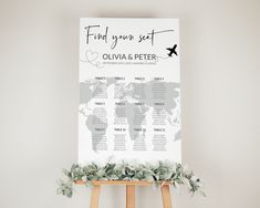 a wedding seating chart with greenery on an easel in front of a white wall