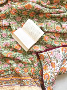 an open book laying on top of a bed next to a blanket and pillow cover