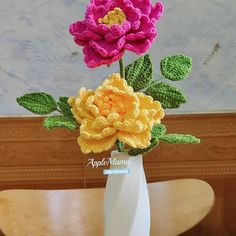 two crocheted flowers in a white vase on a table