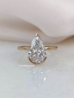 a pear shaped diamond engagement ring sitting on top of a white cloth