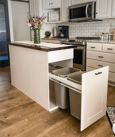 an open cabinet in the middle of a kitchen with stainless steel appliances and white cabinets