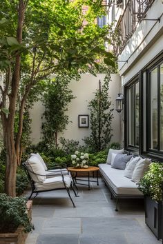 Cozy patio garden with white cushioned seating, surrounded by lush greenery and tall trees. Backyard Patios And Decks, Raised Patio Design, Simple Courtyard Ideas, Apartment Patio Aesthetic, Courtyard Backyard Ideas, Small Concrete Backyard Ideas, Dark Patio Ideas, Patio Sitting Area Ideas