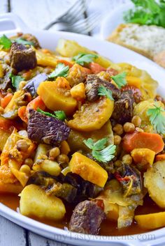 a white bowl filled with vegetables and meat on top of a table next to bread