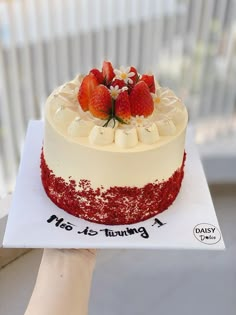 someone holding up a cake with strawberries on top