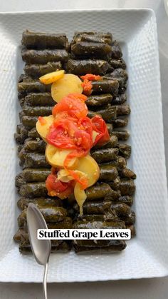 a white plate topped with grape leaves covered in toppings and a serving utensil