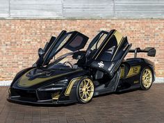 a black and gold sports car parked in front of a brick wall with its doors open