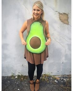 a woman standing in front of a white wall holding an avocado shaped pillow