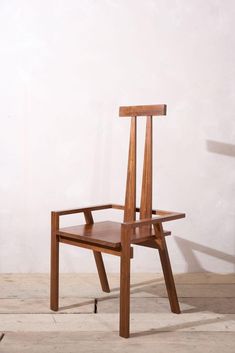 a wooden chair sitting on top of a floor next to a white wall and a black cat