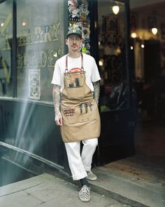 a man in an apron and hat is standing on the sidewalk outside of a store