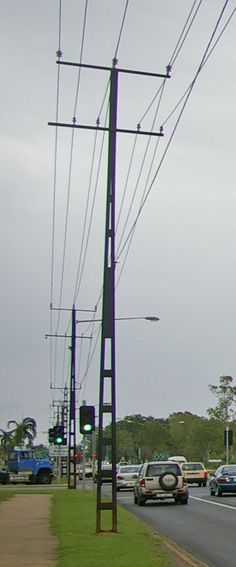 many cars are driving down the road near power lines and traffic lights on an overcast day