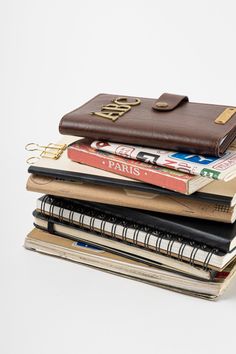 a stack of notebooks and books with a brown leather wallet on top of them