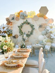 a table set up for a party with balloons and flowers on the wall behind it