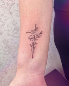 a small flower tattoo on the left inner forearm and wristband, with cross at the top