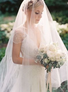 a woman in a wedding dress and veil holding a bouquet with white flowers on it