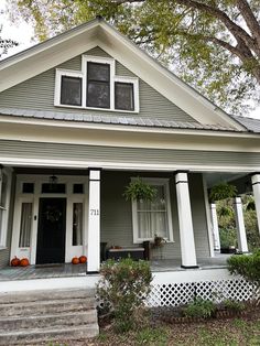 a gray house with white trim and black door on the front porch is surrounded by trees