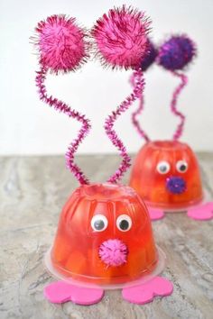 two plastic cups with pink decorations on them and one has googly eyes, while the other has purple pom - poms