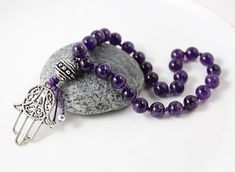 A deep purple Amethyst mini mala will easily fit into a pocket/purse/yoga bag. The perfect tool for stress relief! You don't have to be into meditation to appreciate the soothing feel of this polished natural stone in your hand. Perfect for keeping with you all day long or at your bedside for a few moments of quiet retreat, meditation or affirmation practice. SIZE/LENGTH: Silver healing hand pendant measures approx. 35mm (1 3/8 inches); The beaded portion of this small pocket mala measures appro Spiritual Purple Spacer Beads, Spiritual Purple Polished Beads, Purple Beaded Necklaces With 8mm Beads As Gift, Purple Beaded Necklace With 8mm Beads As Gift, Purple Beaded Necklaces With 8mm Beads For Gifts, Purple 8mm Bohemian Beads, Yoga Beads, Worry Beads, Knotted Mala