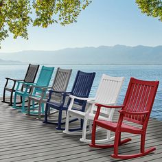 four different colored rocking chairs sitting on a dock