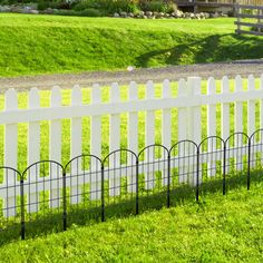 a white picket fence in front of a green yard with grass on the ground and a house in the background