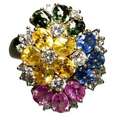 A dazzling and colorful cocktail ring done in 18K yellow gold set with buff-top natural blue, pink, green and yellow sapphires. Total approximate sapphire weight is 6.50cttw. Peppered throughout is another .70cttw in G-H color Vs2-Si1 clarity round diamonds. Dimensions/Weight: Ring measures .95” top to bottom and weighs 12.6g. Size 7 (sizable). Condition: All stones are secure and free of damage. Perfectly wearable condition. R-CNYE Floral Cocktails, Colorful Cocktails, Yellow Gold Setting, Yellow Sapphire, Gold Set, Sapphire Diamond, Cluster Ring, Cocktail Rings, Round Diamonds