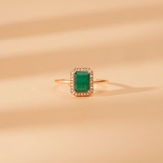 an emerald and diamond ring sitting on top of a beige surface with the light shining through it