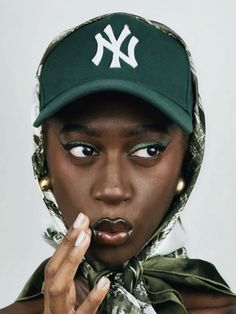 a woman wearing a new york yankees hat and scarf with her finger in her mouth