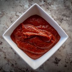 a square white bowl filled with marinara sauce