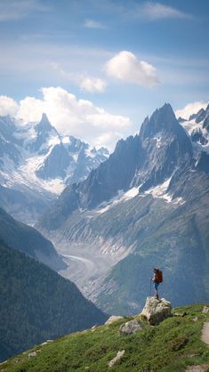 a man standing on top of a lush green hillside with mountains in the back ground