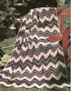 a crocheted blanket sitting on top of a wooden bench next to a tree