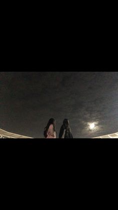 two people standing next to each other on a field at night with the moon in the sky