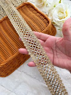 a woman holding onto a gold chain with white flowers in the background and a basket behind her