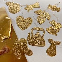 gold foiled christmas ornaments and decorations on a white table with golden wrapping paper next to it