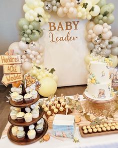 a table topped with lots of cakes and cupcakes next to a baby shower sign